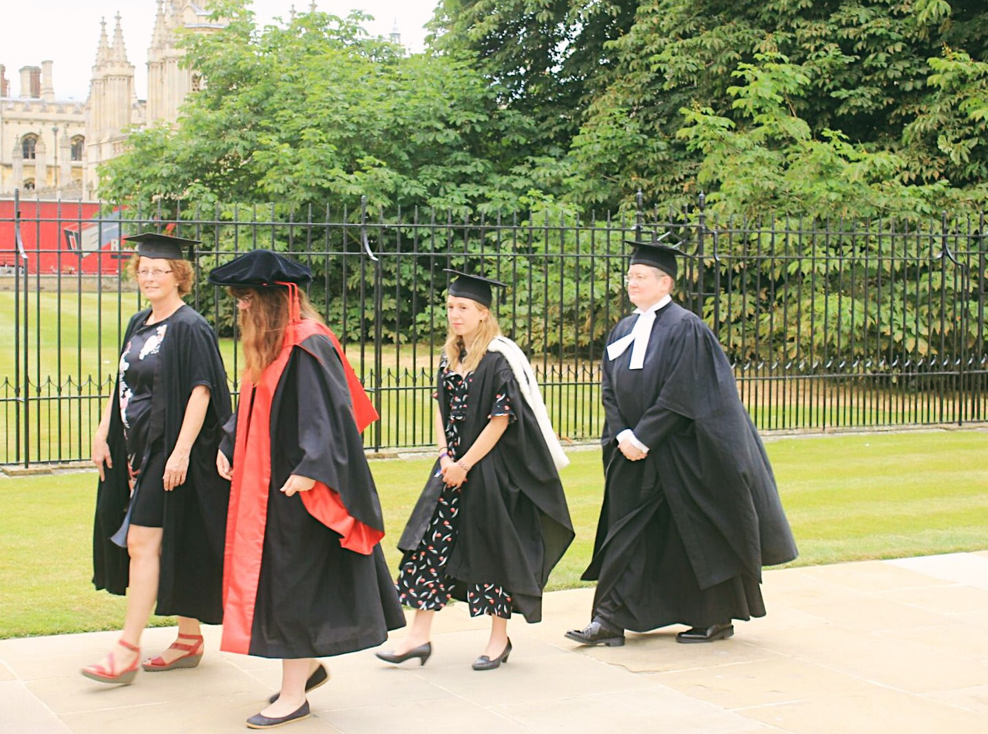 Photo of four people walking, wearing Cambridge ceremonial gowns